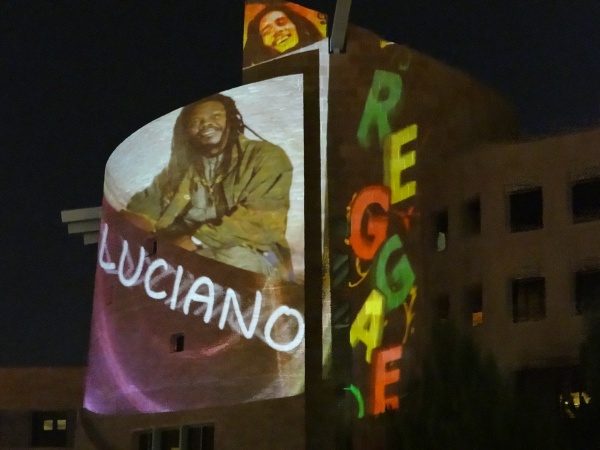 Luciano on stage with his album cover projected onto the building behind him